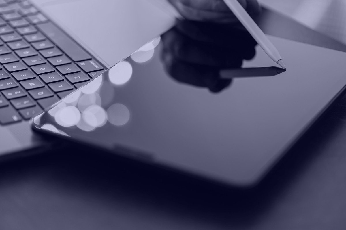 Tablet mit Stift neben aufgeklappter Laptop-Tastatur